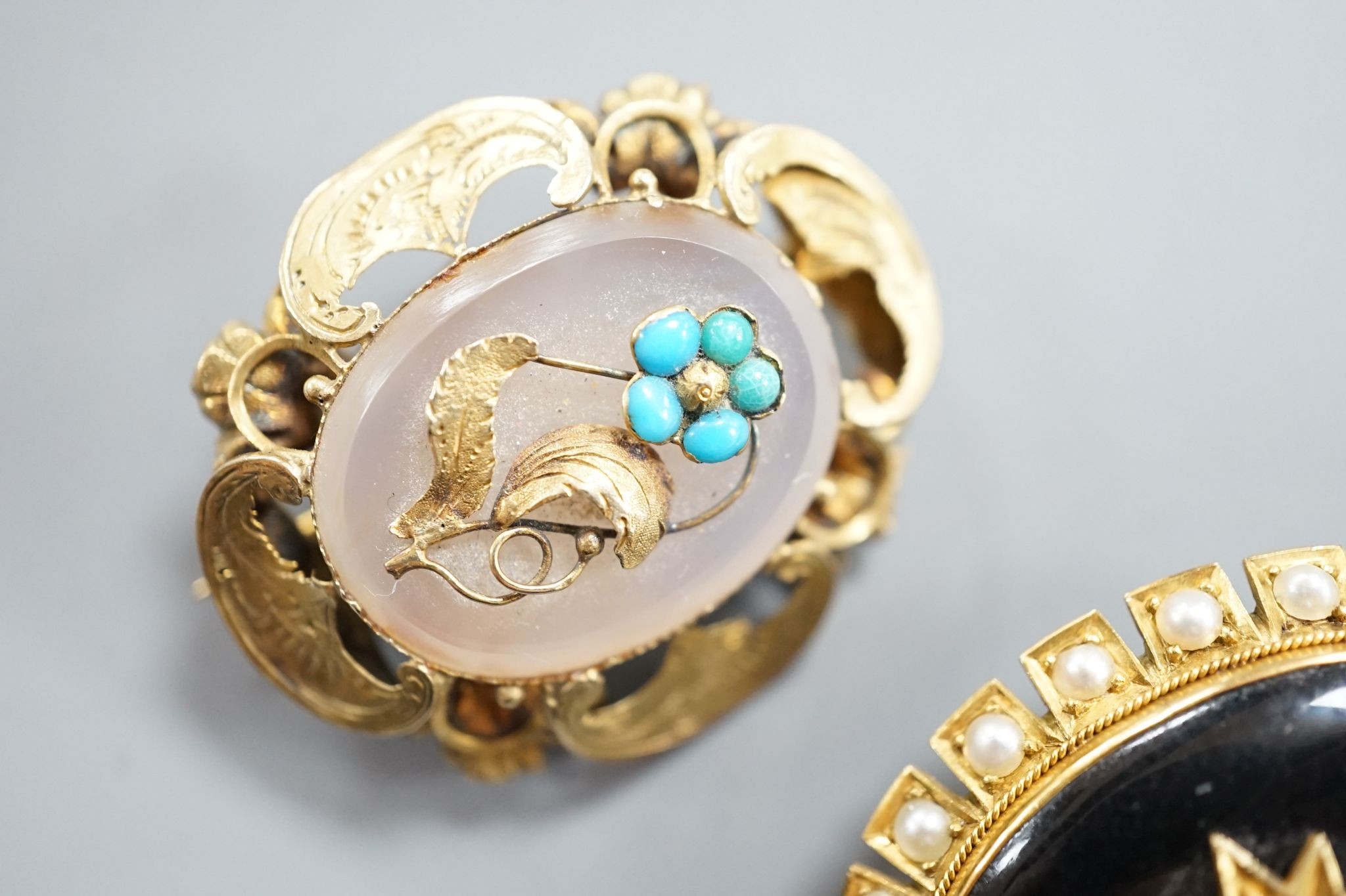 Two Victorian yellow metal and gem set oval brooches, including black enamel and split pearl, largest 34mm.